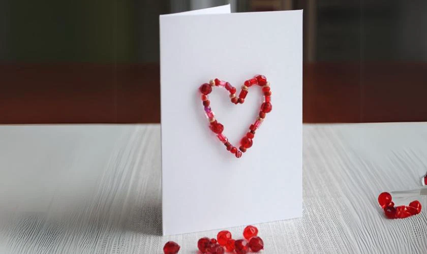Dùng keo nến gắn hình trái tim kết từ hạt gỗ lên thiệp rồi để khô
